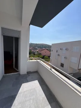 Covered balcony with a metal railing and a view of surrounding buildings and a hill. - image 10