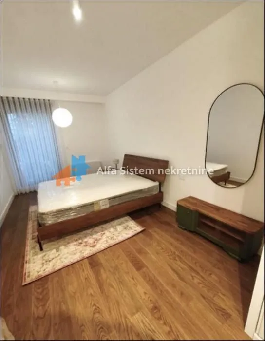 A bedroom with a double bed, wooden dresser, and a wall mirror.