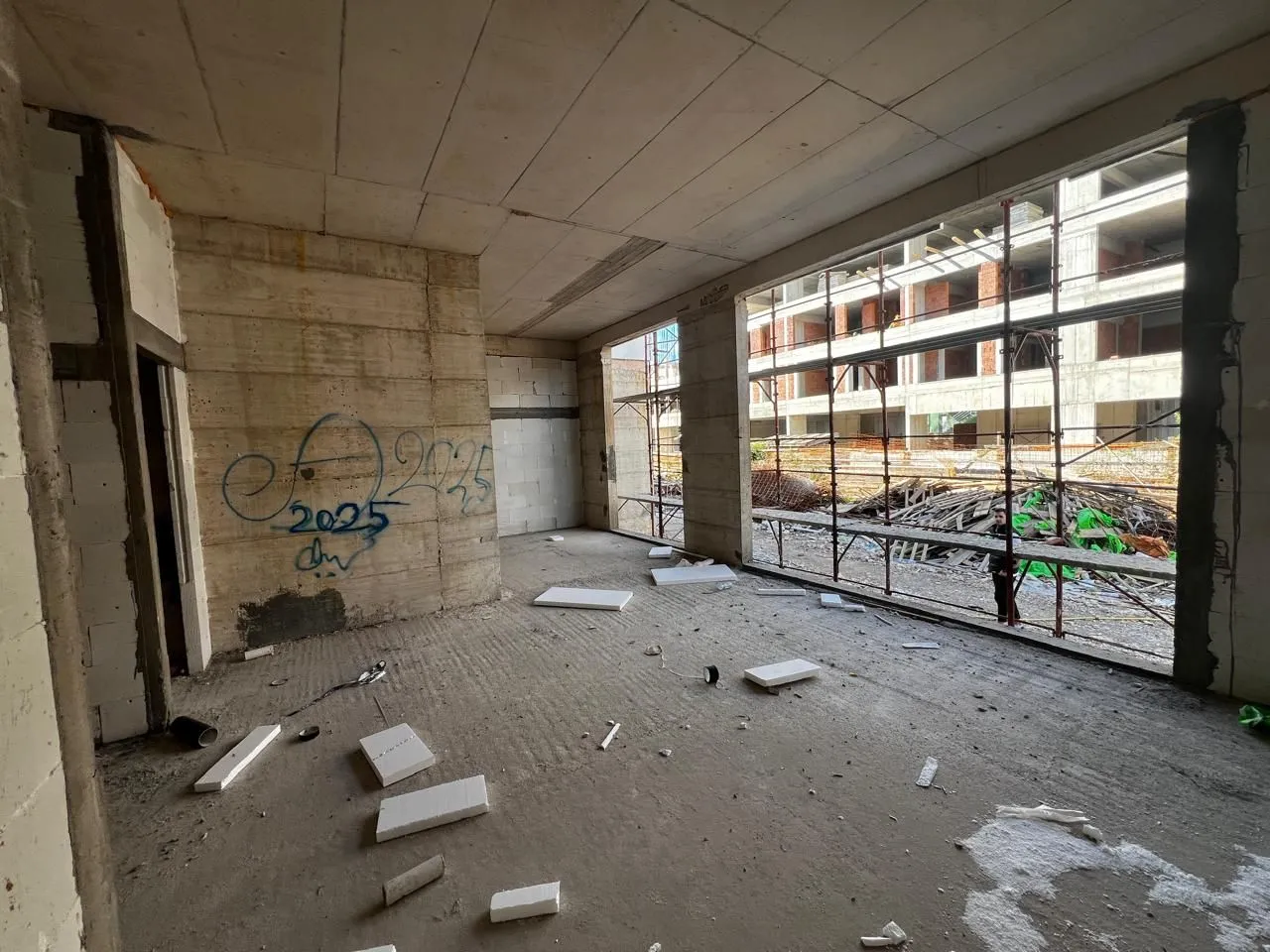 Unfinished room in grey phase under construction with large windows and a view of the construction site.