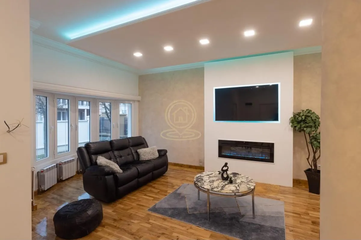 Living room with a black leather sofa, wall-mounted television, and a fireplace.