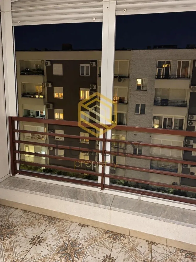 Zastakljena terasa sa pogledom na okolne zgrade u noćnim satima.