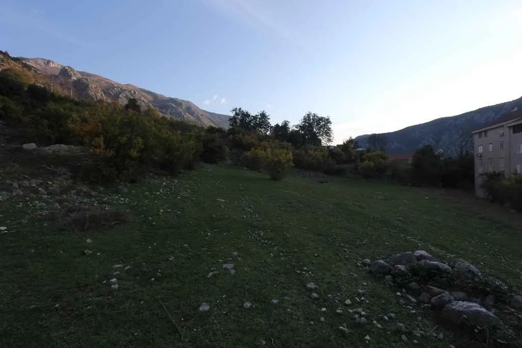 Zeleni plac na blagoj padini okružen planinskim pejzažem.
