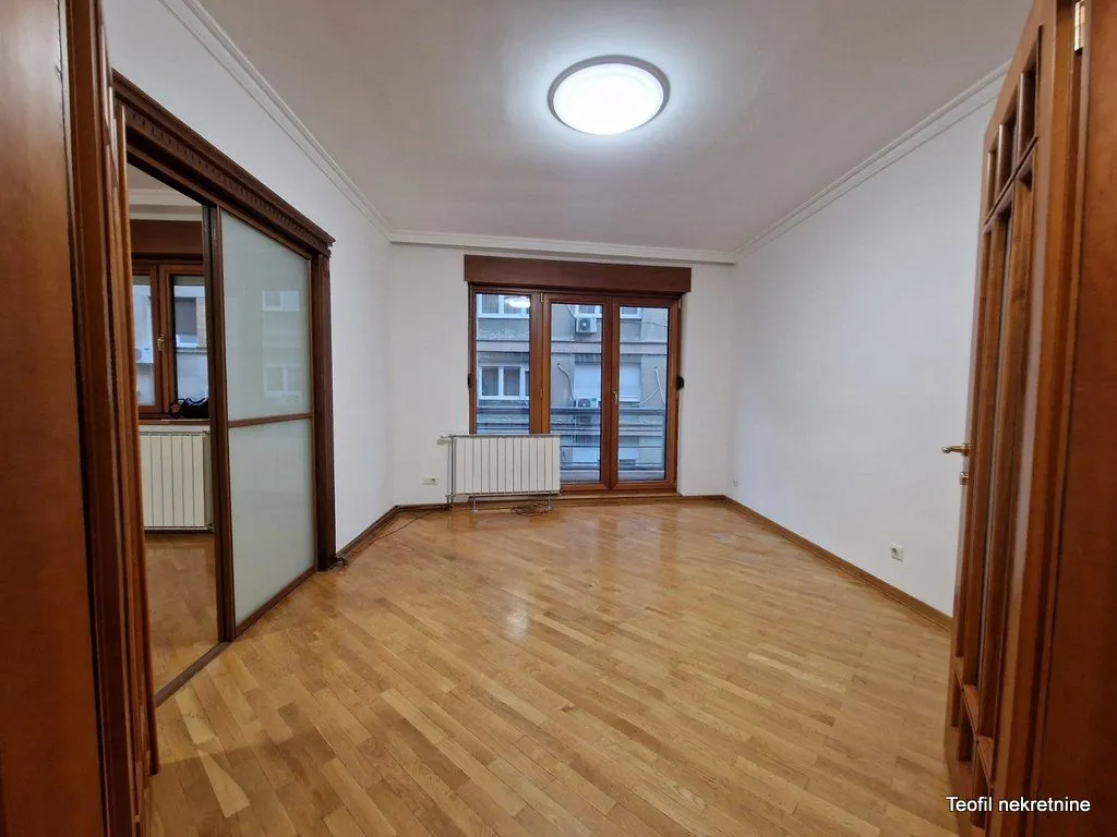 Empty room with wooden parquet flooring and balcony doors.