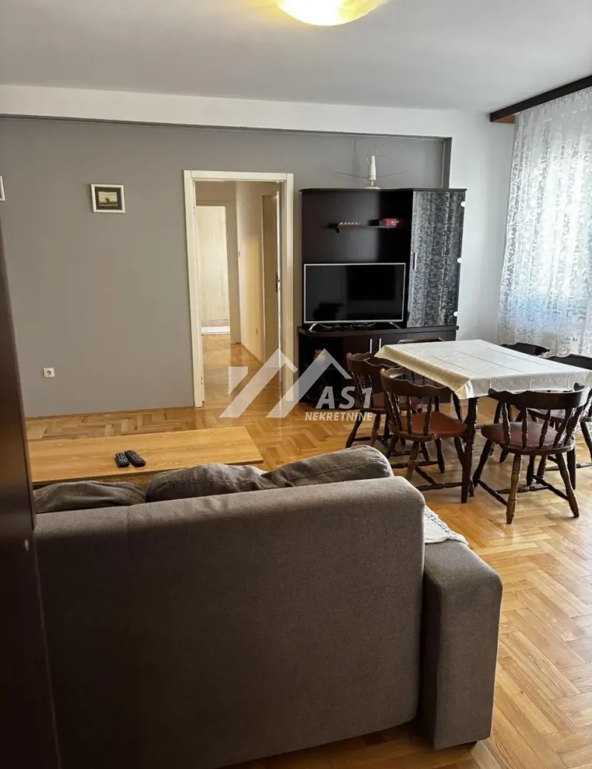 Living room with a sofa, dining table, and parquet flooring.