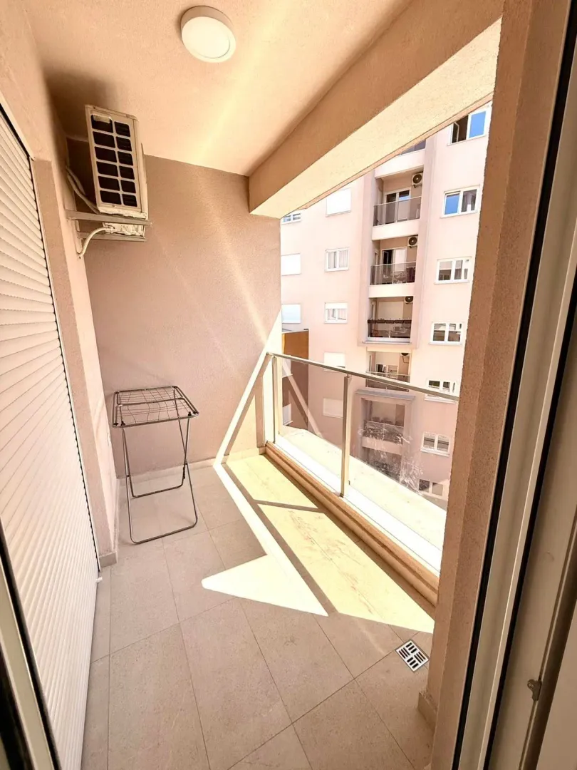 A bright balcony with a glass railing and tiled floor.