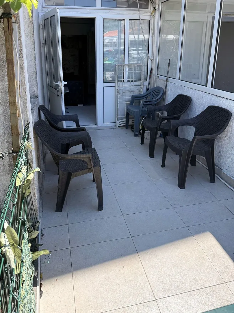 Zastakljena terasa sa crnim plastičnim stolicama i izlazom u enterijer.