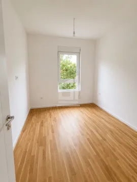 Empty room with white walls, wooden parquet flooring, and a window. - image 2