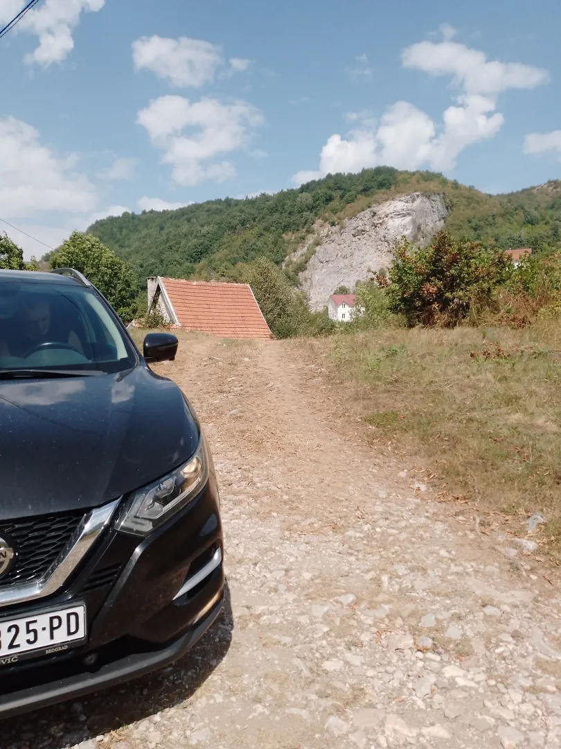 Pogled na prilaz i okolni pejzaž sa automobilom u prvom planu.