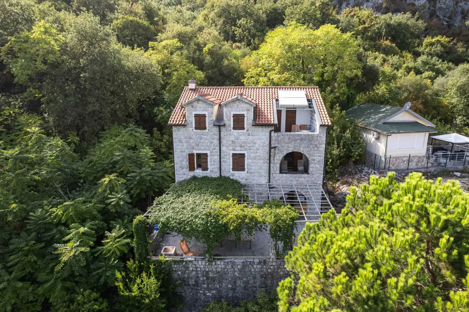 Pogled iz vazduha na kamenu kuću okruženu zelenilom.