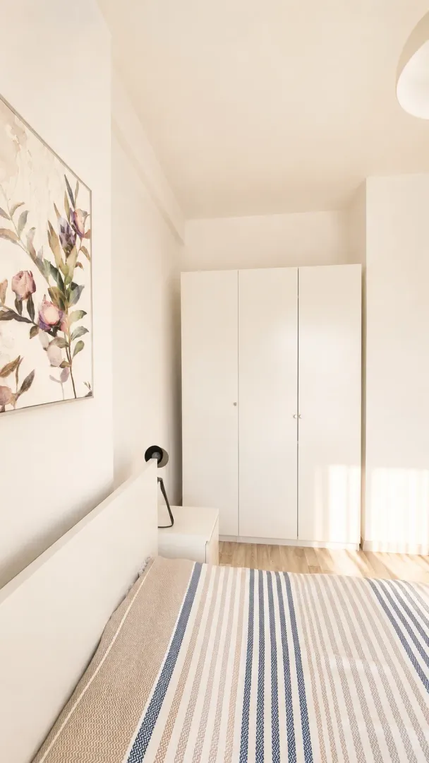 Bright bedroom with a white bed, wardrobe, and a painting on the wall.