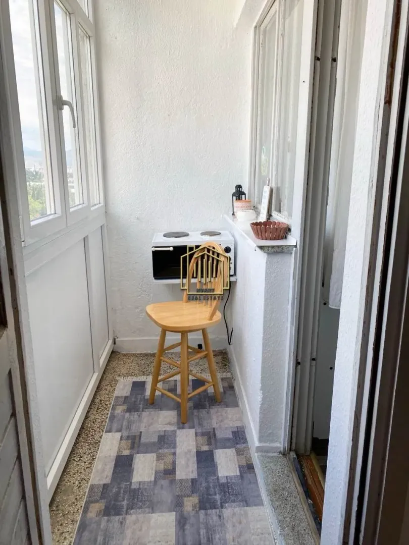 Enclosed balcony with a chair and a small kitchenette unit.