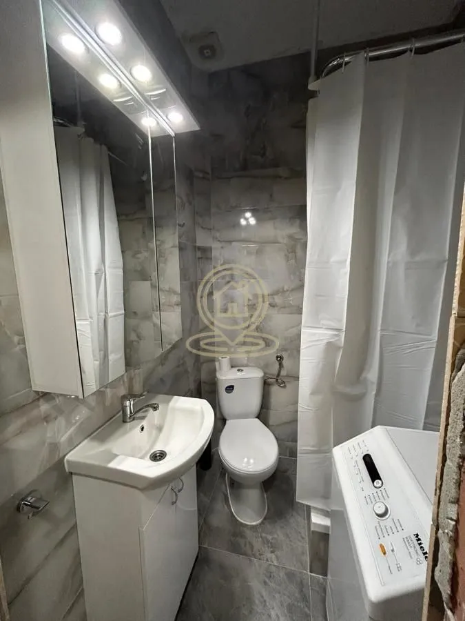 Compact bathroom with a sink, toilet, shower cabin, and washing machine.