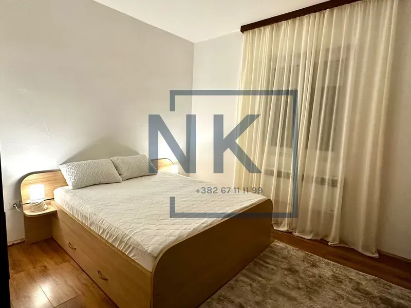 Furnished bedroom with a double bed, bedside tables, and a window with curtains.