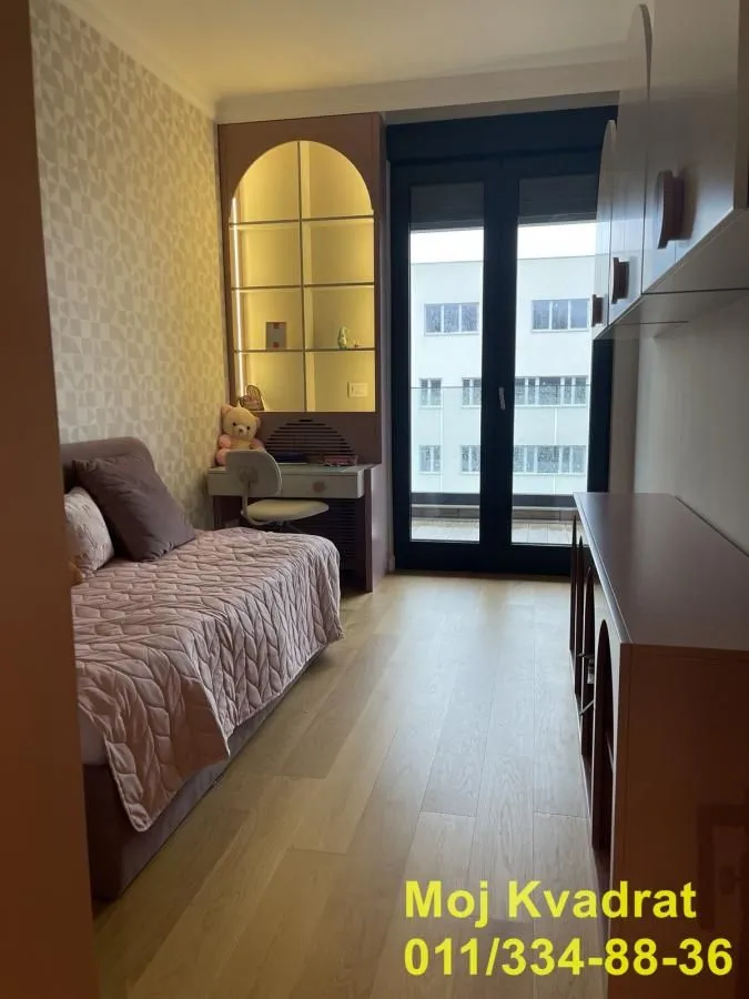 Dečja soba sa krevetom, radnim stolom i balkonskim vratima.