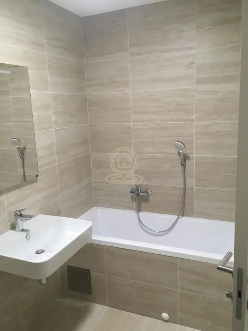 Bathroom equipped with a bathtub, washbasin, and mirror, tiled in beige ceramic tiles.