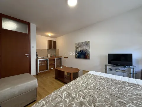 Small living room with a bed, TV, and kitchen units in the corner. - image 3