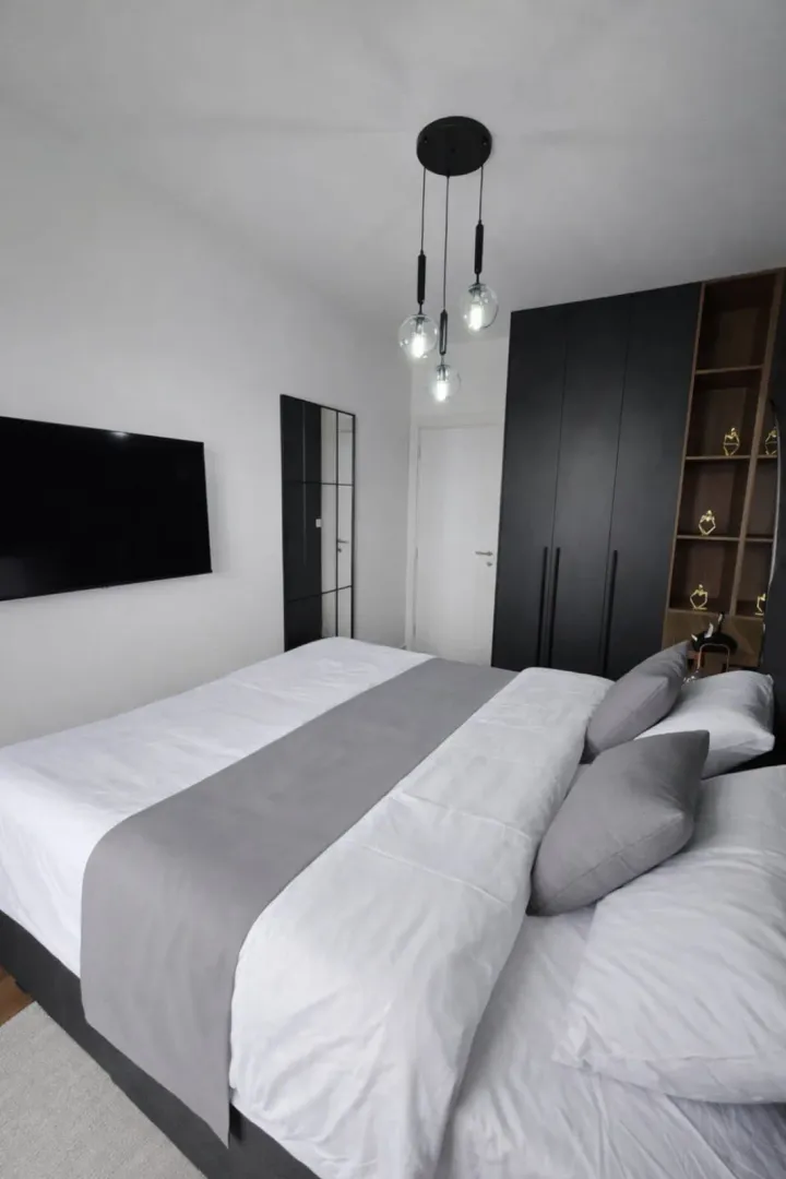 Modern bedroom with a double bed, black wardrobe, and wall-mounted TV.