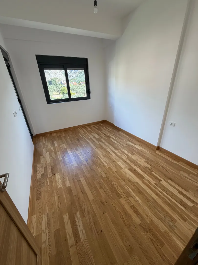 Prazna soba sa drvenim podom i prozorom koji gleda na prirodu.