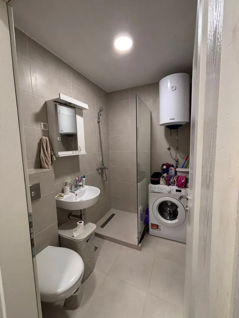 Smaller bathroom with a walk-in shower, washbasin, and washing machine.