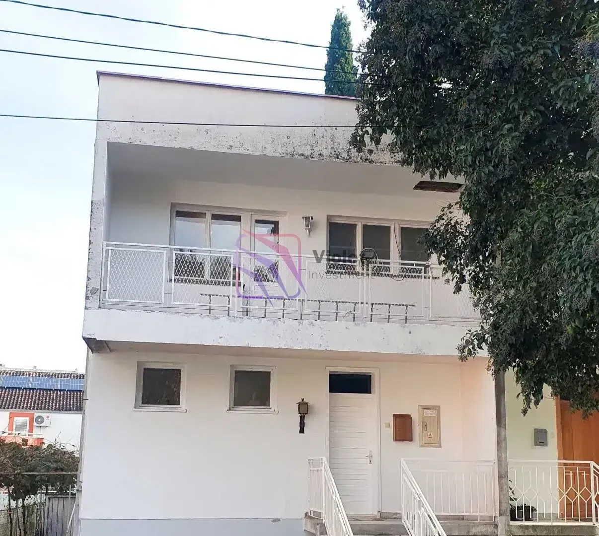 Prednji pogled na višespratnu kuću sa balkonom i ulaznim vratima.