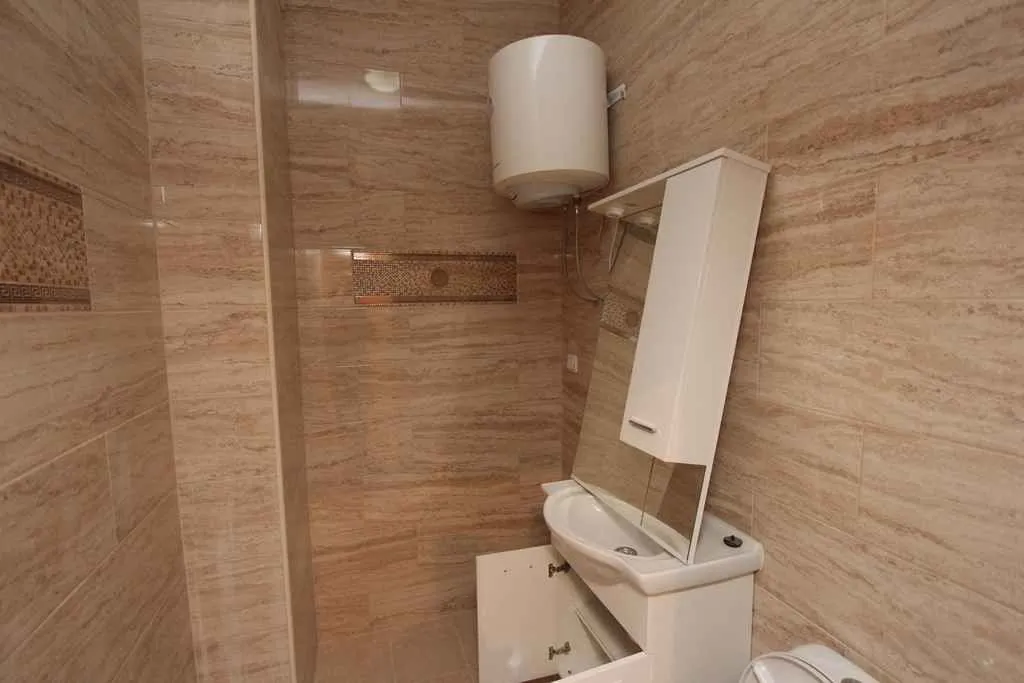Kupatilo sa svijetlim pločicama, lavaboom i bojlerom.