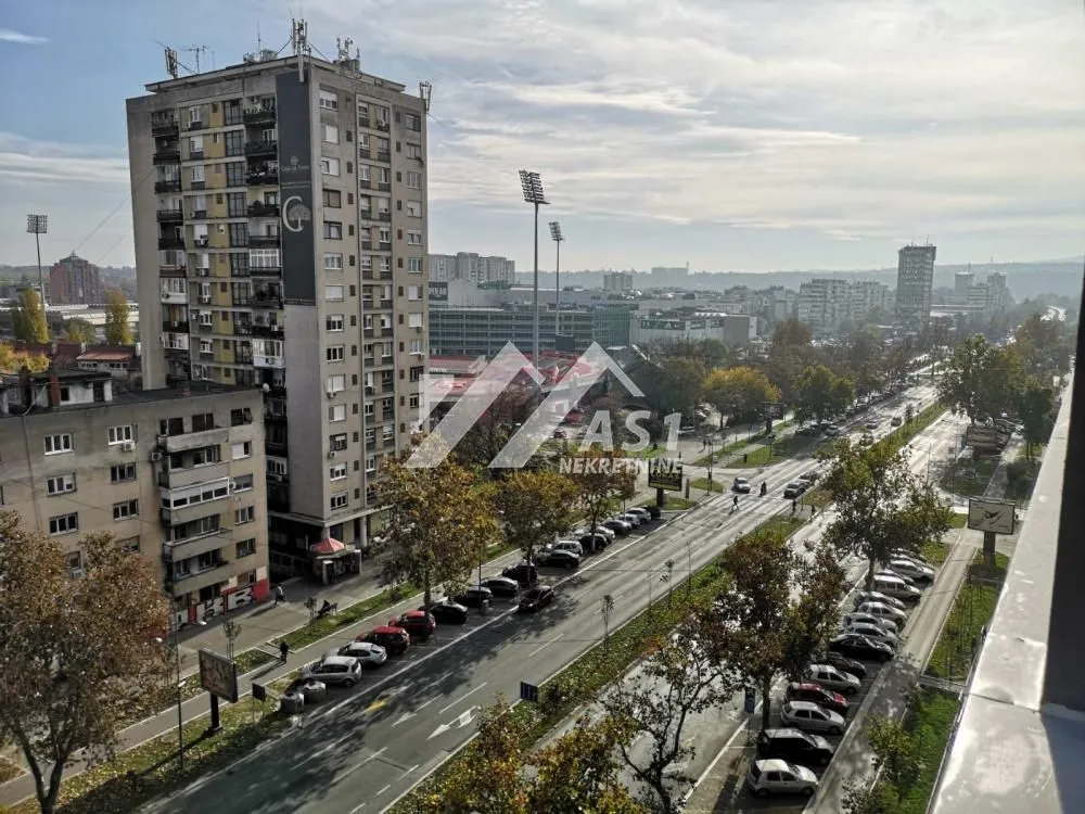 Pogled sa prozora na ulicu, parkirana vozila i okolne zgrade.