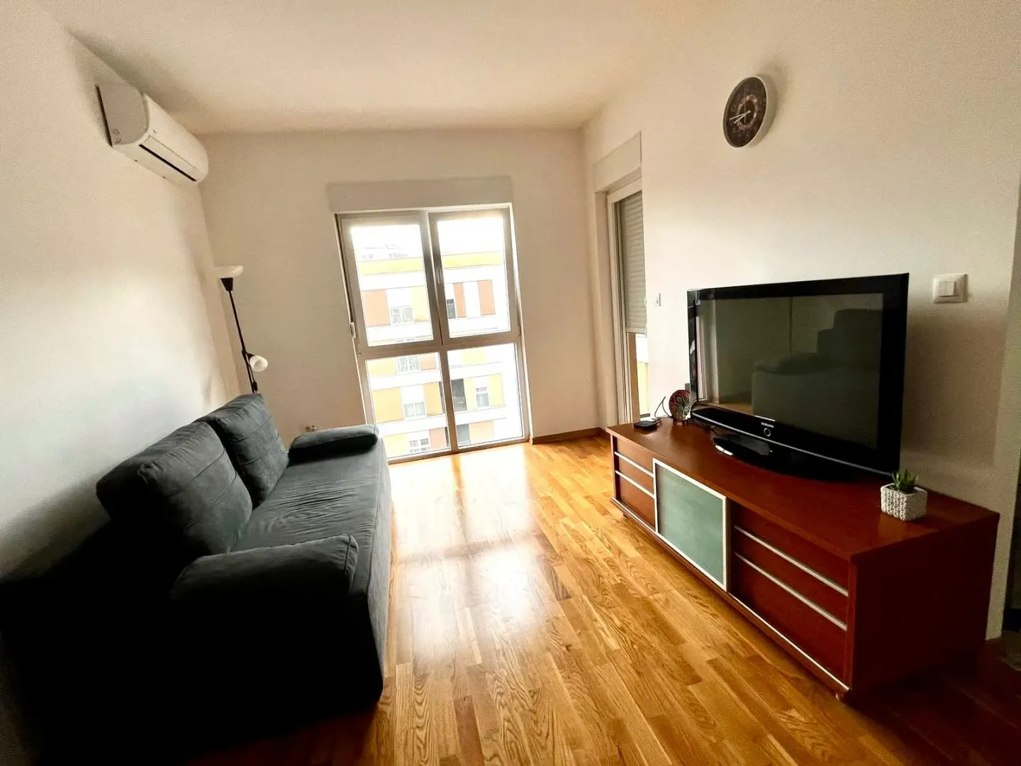 Dnevna soba sa garniturom, TV komodom i drvenim podom.