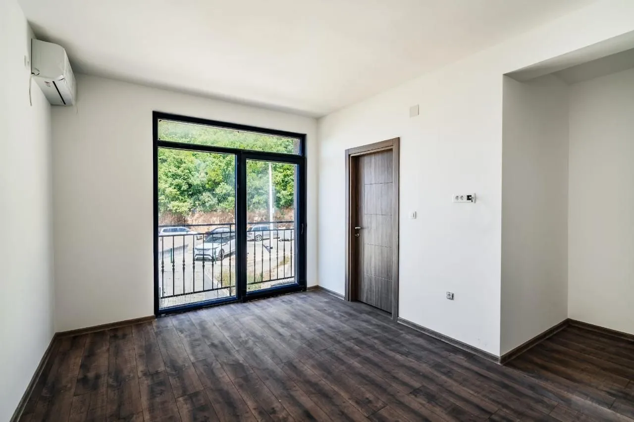 Empty room with dark wooden flooring and balcony doors.