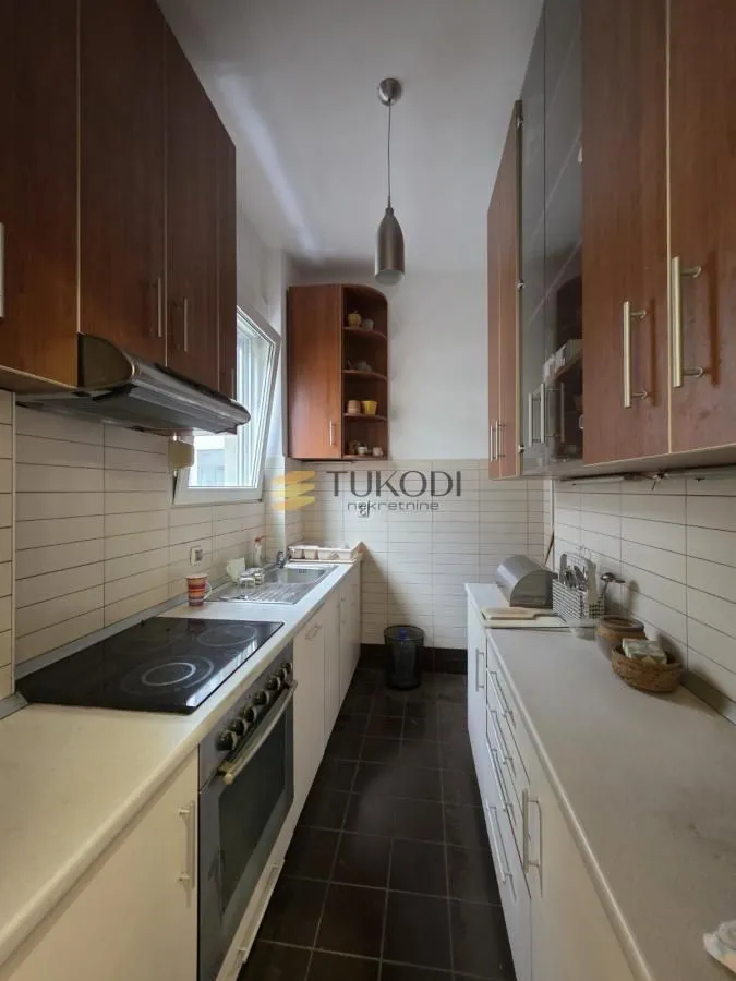 Narrow kitchen with wooden cabinetry, white countertops, and built-in appliances.