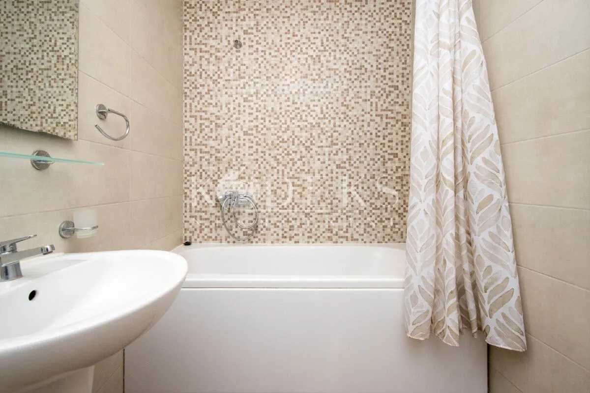 Bathroom with a bathtub, washbasin, and mosaic tiles on the wall.