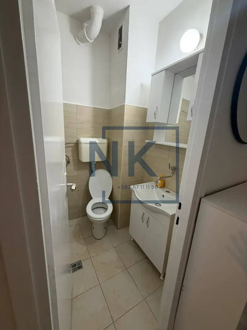 Manje kupatilo sa wc šoljom, umivaonikom i visećim elementom sa ogledalom.