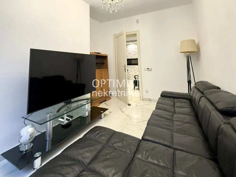 Living room with a black sectional sofa, television, and floor tiles.
