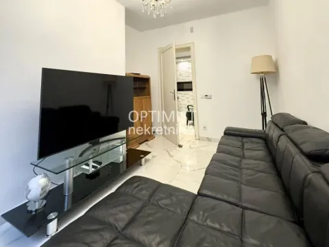 Living room with a black sectional sofa, television, and floor tiles. - image 6