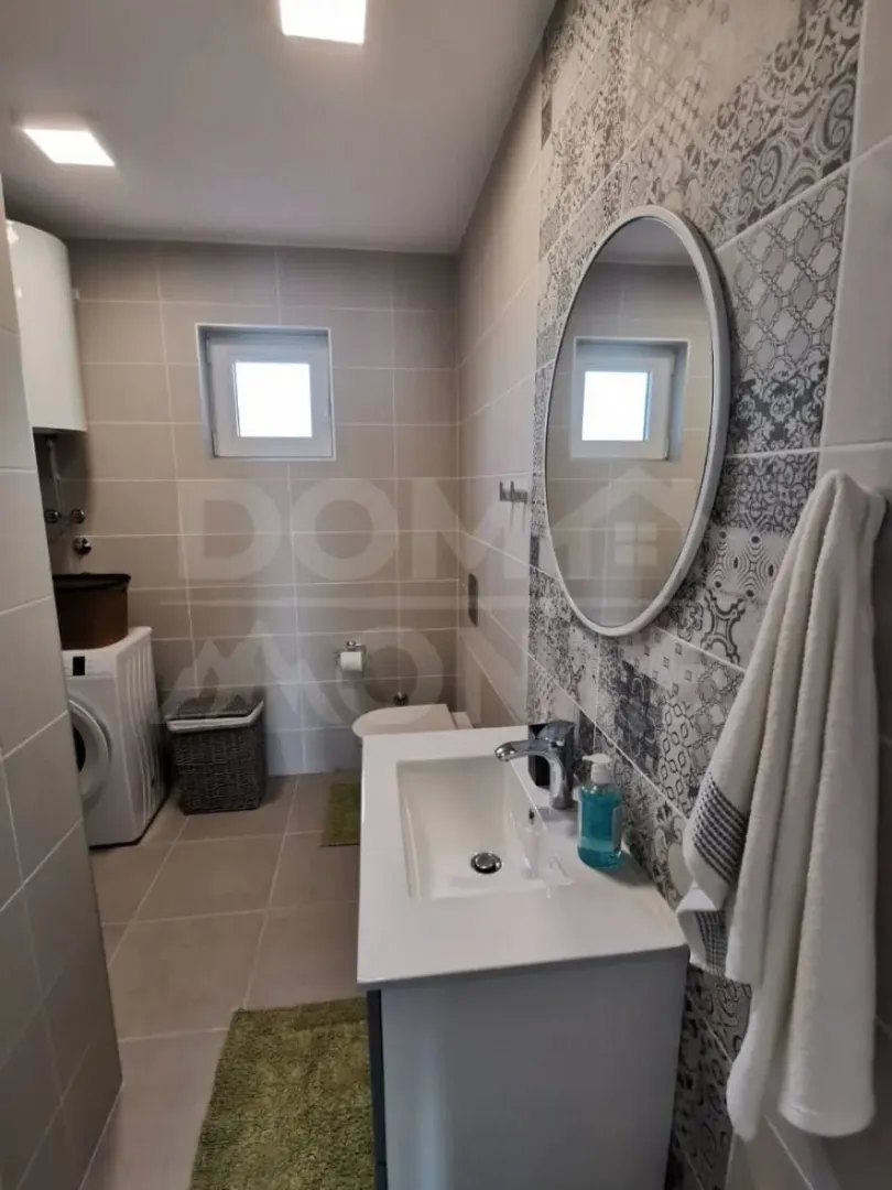 Modern bathroom equipped with a sink, washing machine, and shower.