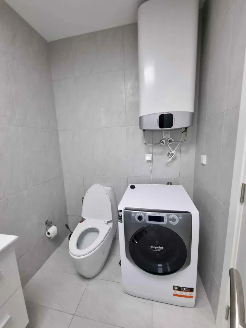 Kupatilo opremljeno toaletom, veš mašinom i bojlerom na zidu.