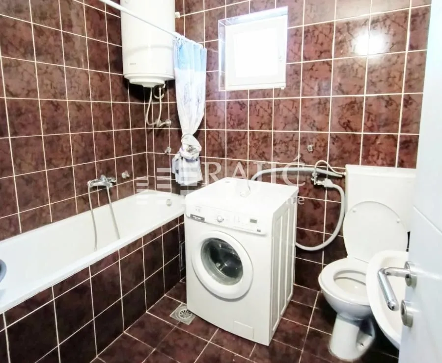 Bathroom tiled in brown with a bathtub, washing machine and sanitary fixtures.