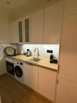 Manja moderna kuhinja sa belim elementima, drvenom radnom površinom i ugrađenom mašinom za veš. - image 7