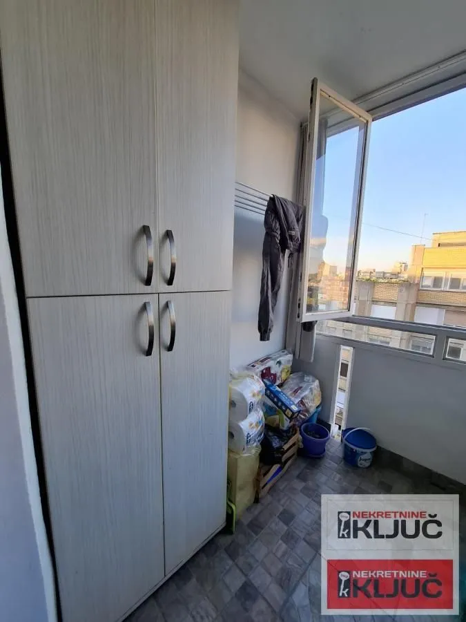 Zastakljeni balkon sa ormarom i pogledom na grad.