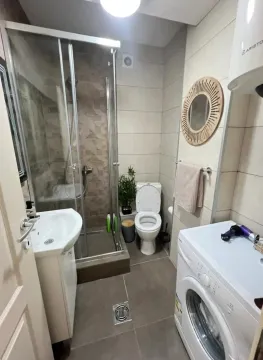 Small bathroom with a shower cabin, washbasin, toilet, and washing machine. - image 6