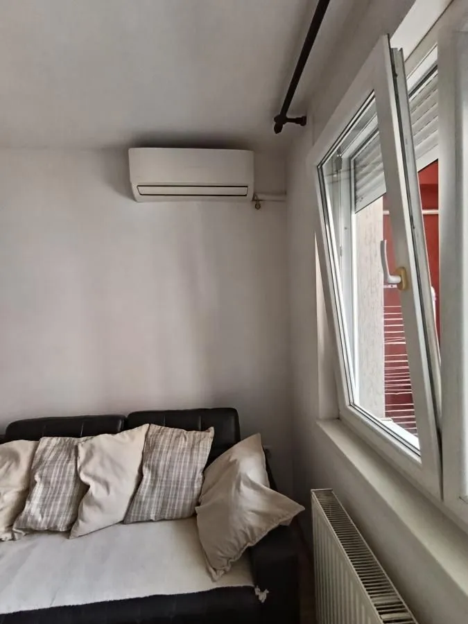 Pogled na deo dnevnog boravka sa kaučem, klima-uređajem i otvorenim prozorom.