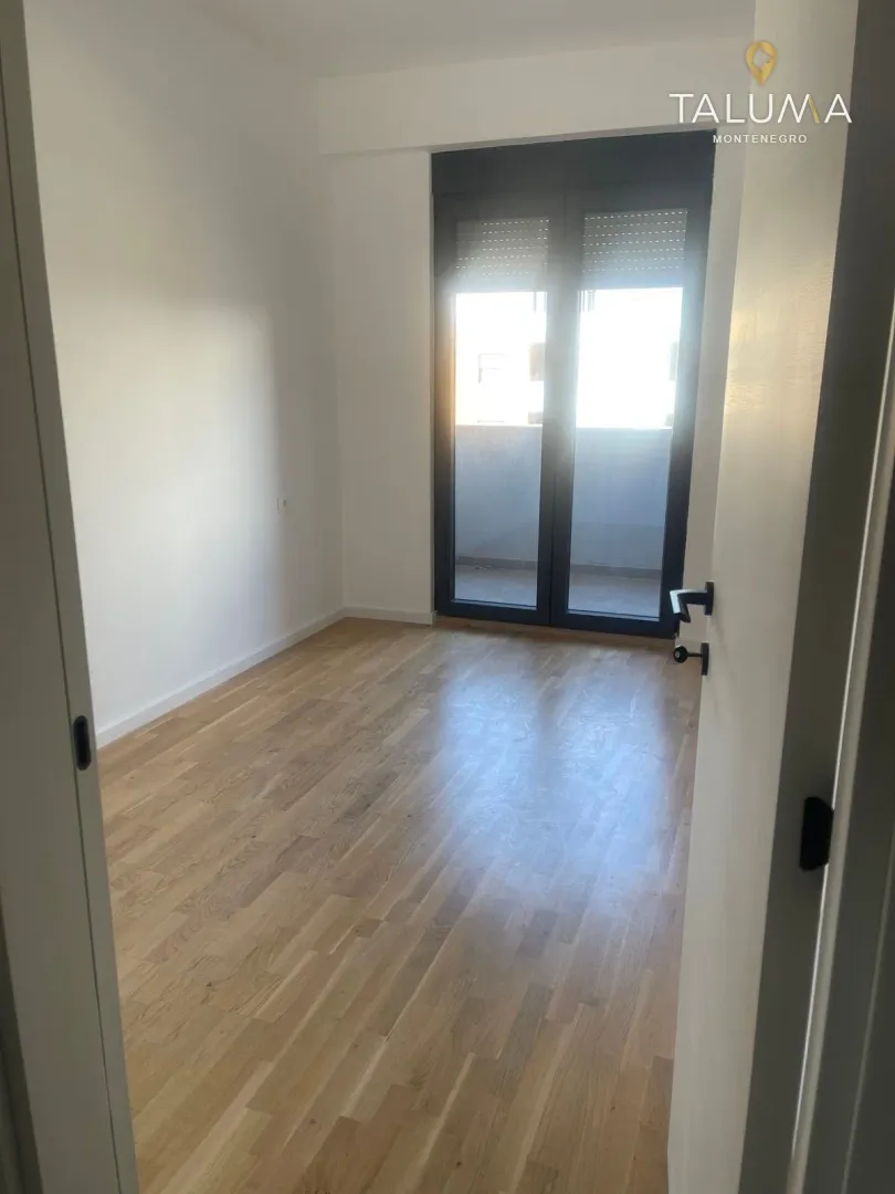 View through an open door into an empty room with hardwood floors and balcony doors.