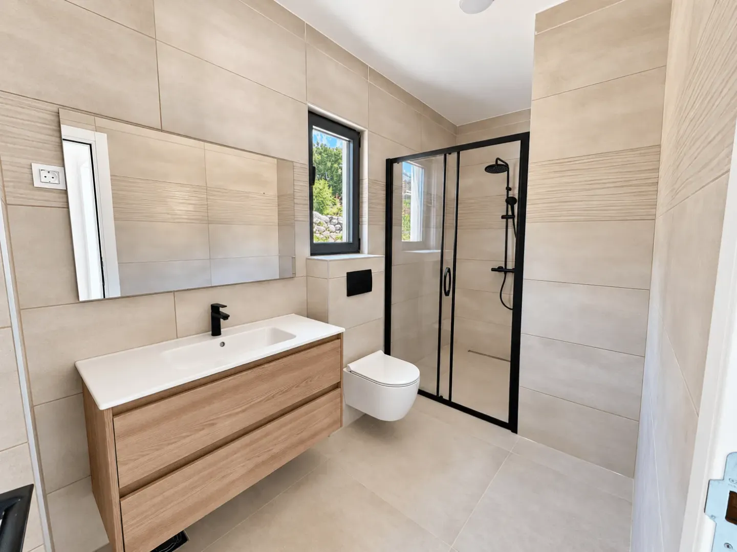 Modern bathroom with a walk-in shower, vanity and toilet in beige tones.