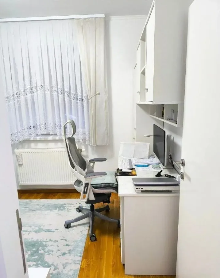 Radna soba sa radnim stolom, računarom i belim nameštajem.