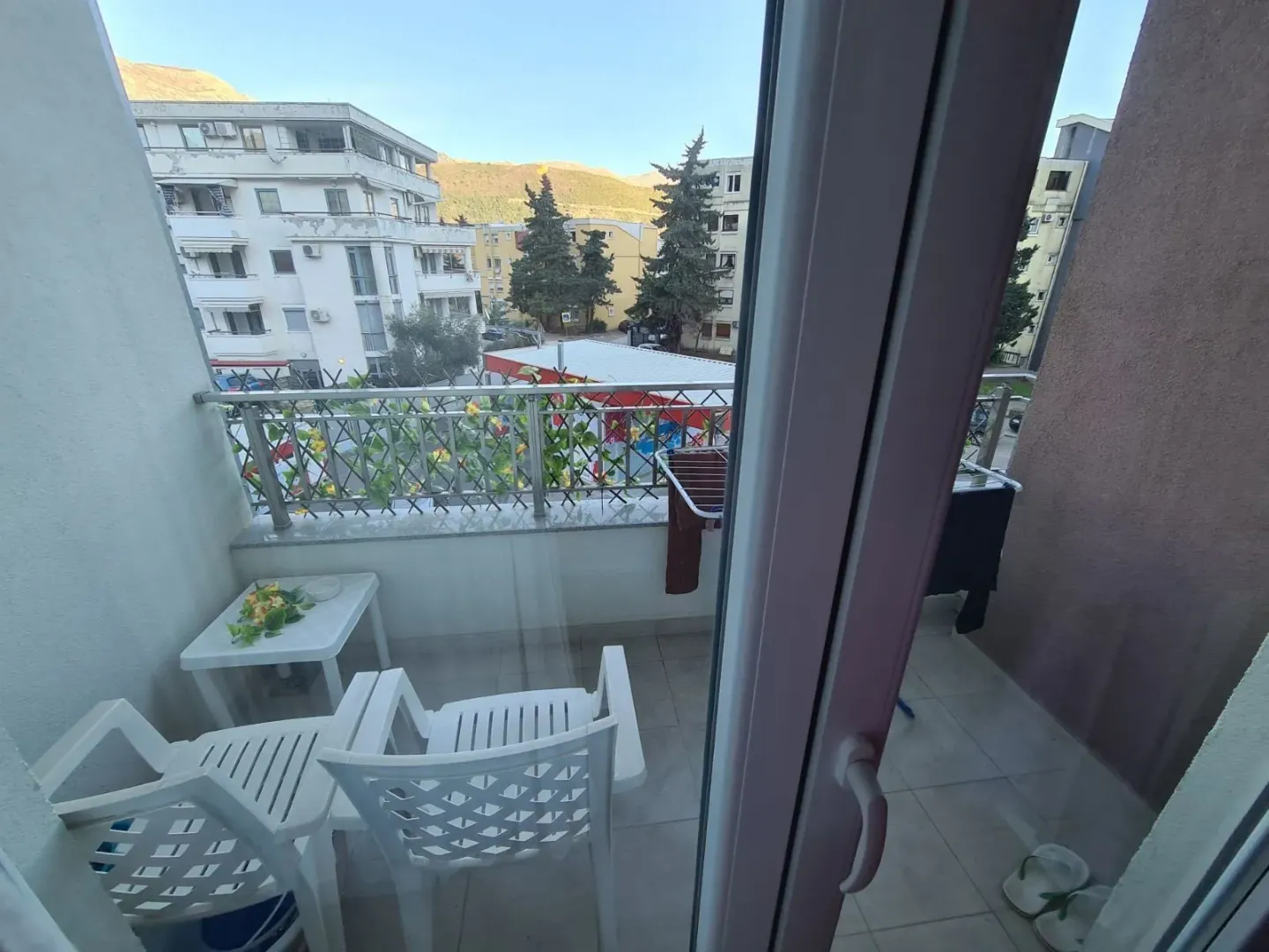 Small furnished balcony with seating furniture and a view of surrounding buildings and hills.