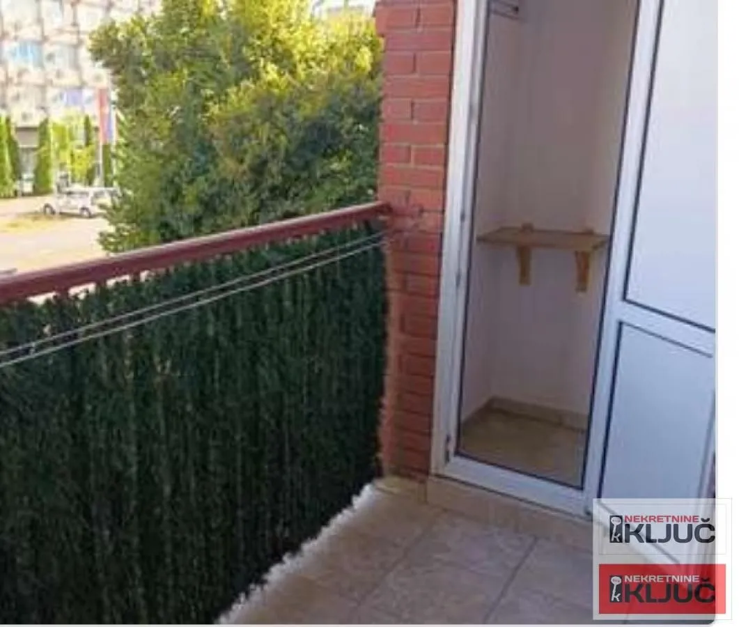 Balkon sa zelenom ogradom i pogledom na ulicu.