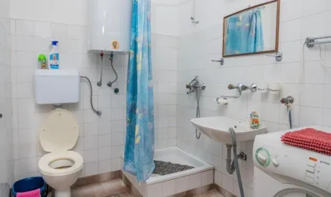 Manje kupatilo sa bijelim pločicama, tuš kabinom, lavaboom i toaletom. - image 7