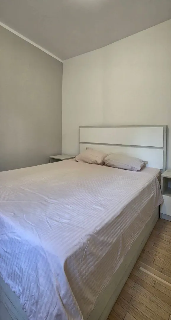 Uredna spavaća soba sa bračnim krevetom i bijelim noćnim stočićima.
