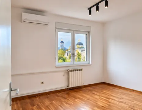 Prazna soba sa drvenim podom, klima uređajem i pogledom kroz prozor. - image 4