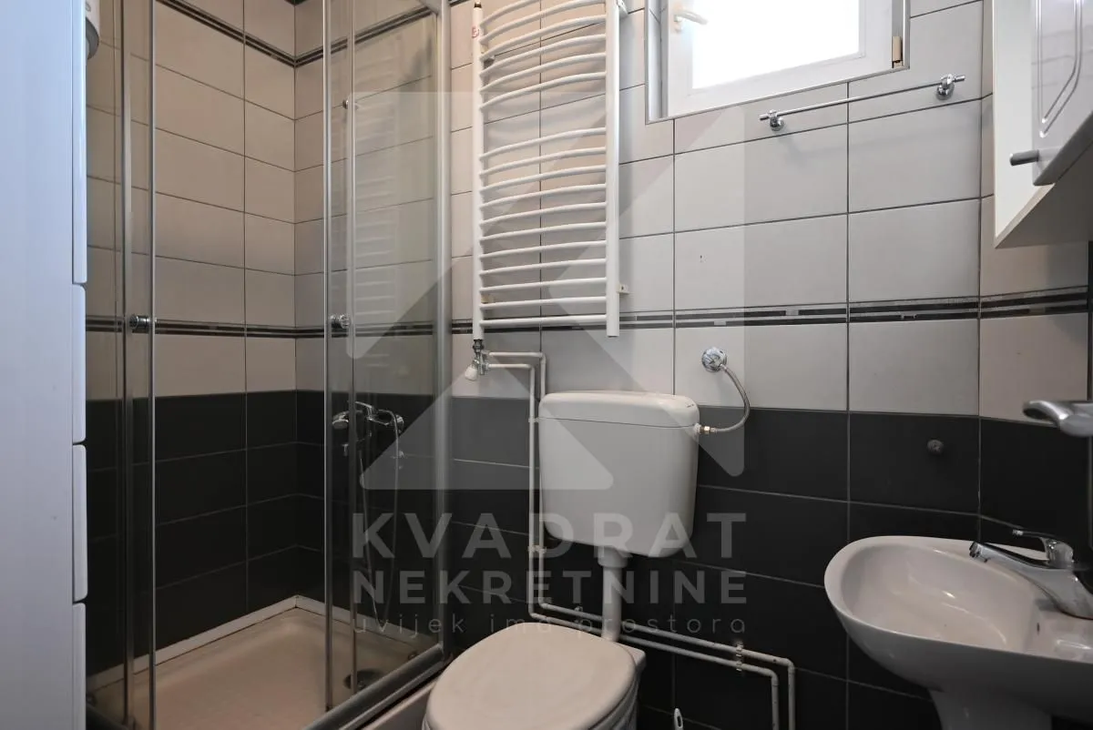 Smaller bathroom with a shower cabin, toilet, and sink.