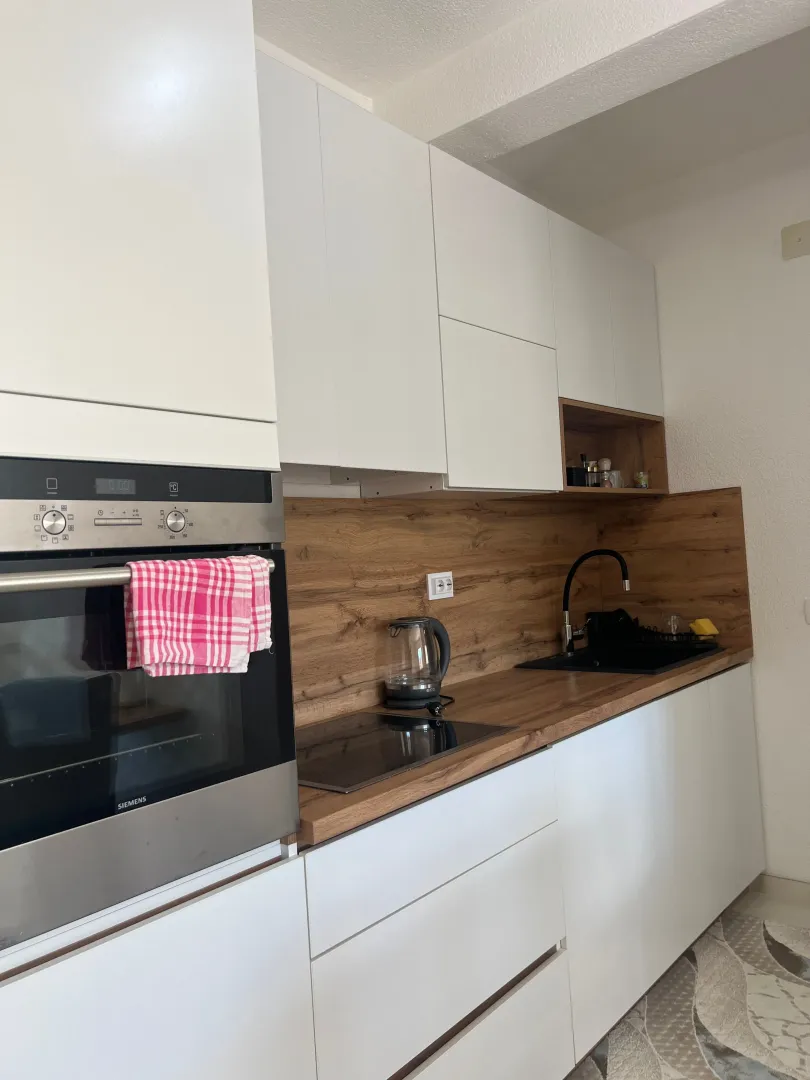 Modern white kitchen with wooden elements and a built-in oven.